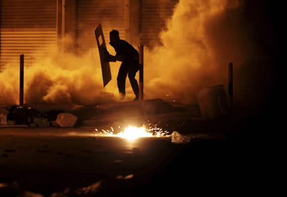 A Bahraini anti-government protester carrying a makeshift shield reacts to tear gas fired by riot police during clashes in Diraz, Bahrain.