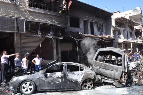 This photo released by the Syrian official news agency SANA, Syrian citizens gather near damaged cars that were burned after a car bomb exploded in the suburb of Jaramana, Damascus, Syria.