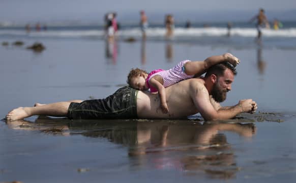 A man rests with his daughter on the beach under sunny skies in Coronado, Calif. Warm weather and blue skies brought summertime crowds to area beaches, with more good weather forecasted on the way.