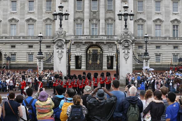 People watch the Changing of the Guard as a notice proclaiming the birth of a baby boy of Prince William and Kate, Duchess of Cambridge is put on display for the public view at Buckingham Palace in London.