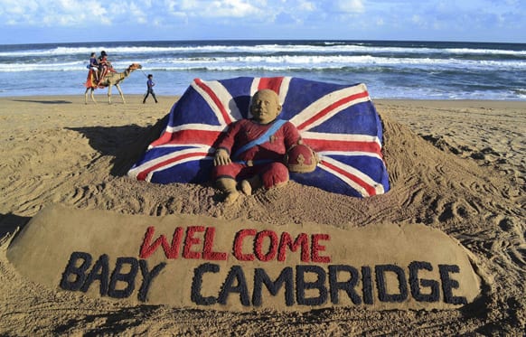 Tourists ride a camel past a sand sculpture created by sand artist Sudarshan Pattnaik to celebrate the birth of the Prince of Cambridge, the son of Britain`s Prince William and Kate, Duchess of Cambridge, at a beach in Puri.