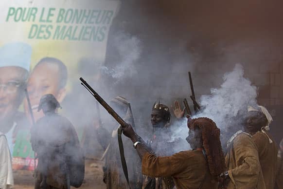 Traditional Dogon hunters fire shotguns to welcome presidential candidate Ibrahim Boubacar Keita, next to one of his campaign posters bearing the slogan