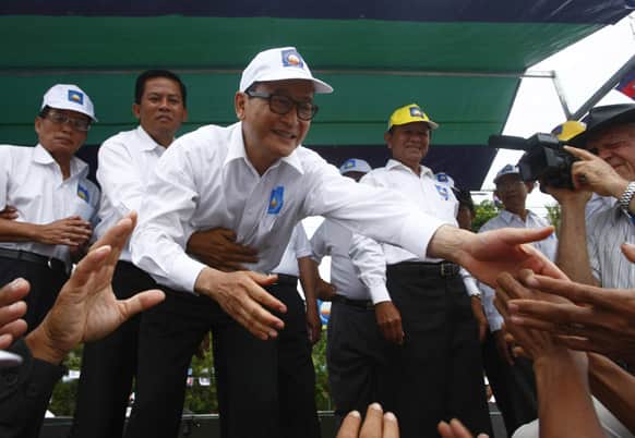 Sam Rainsy, center, president of the Cambodia National Rescue Party shakes hands with his party supporters during an election campaign at Kampong Speu province, west of Phnom Penh, Cambodia.