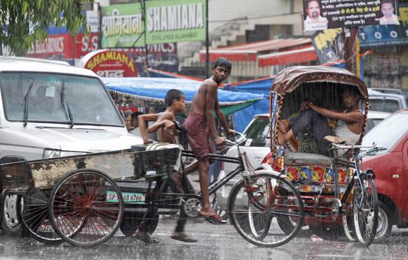 An Indian rickshaw puller rests inside his rickshaw, as a boy rides a cart in the rain in Allahabad.