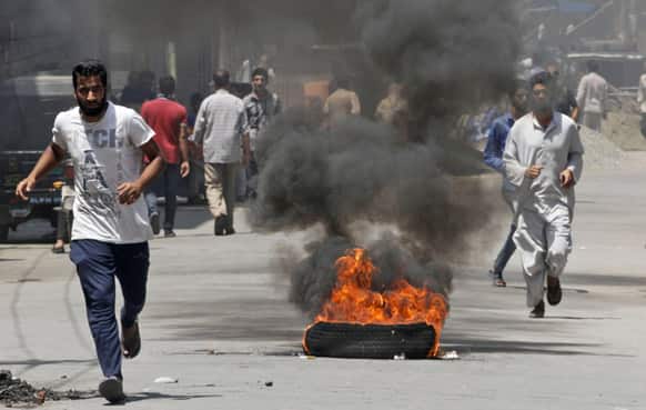 Kashmiris run past a burning tire during a protest against the killing of four villagers, in Srinagar.