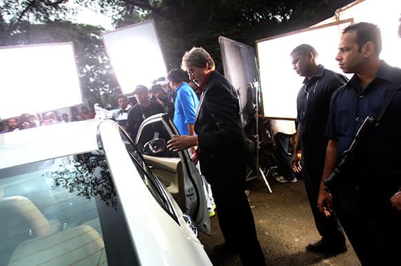 Bollywood actor Amitabh Bachchan, center, stands near a car during a commercial shoot at the film city in Mumbai.