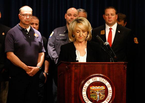 Arizona Gov. Jan Brewer, front, pauses for a moment after she signs a bill into law establishing a memorial for fallen firefighters, in Phoenix. Last month 19 firefighters were killed battling the Yarnell wildfire near Prescott, Ariz.