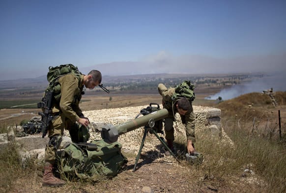 Israeli soldiers cover a rocket at the border with Syria on the Israeli controlled Golan Heights as smoke rises following explosions.