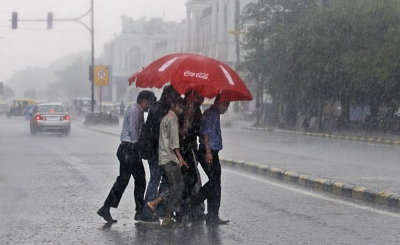 Indians huddle together under an umbrella as they cross a road during heavy downpour in New Delhi.