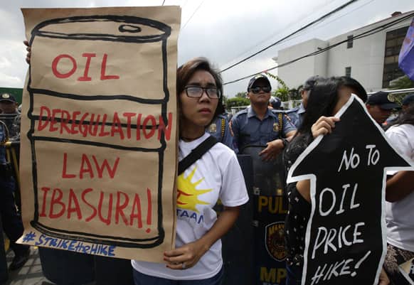 Riot police watch as protesters display placards during a rally outside an oil depot to protest another round of oil price increase implemented by the big three oil companies, in Manila, Philippines.