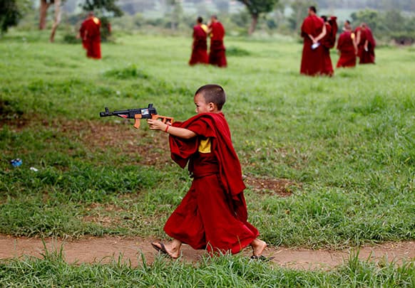 A novice Tibetan Buddhist monk plays with a toy gun during a break from their spiritual leader the Dalai Lama`s religious sermon outside the Gyudmed Tantric Monastery in Gurupura 212 kilometers (132 miles) southwest of Bangalore.