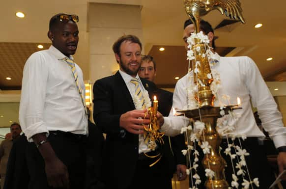 South African cricket captain AB de Villiers, center, lights a traditional lamp with a candle as his teammates Lonwabo Tsotsobe, left, and Farhaan Behardien, second right, watch upon arrival at the team`s hotel in Colombo.