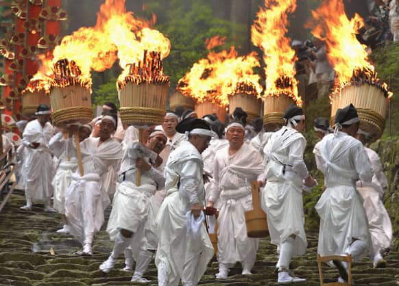 Parishioners carrying giant torches descend a steep stone stairway at a shrine approach during the annual grand fire festival of Kumano Nachi Shrine in Nachi Katsuura.