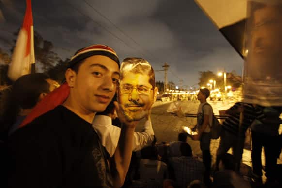A supporter of Egypt`s ousted President Mohammed Morsi poses with a paper mask of Morsi as he and others face the Egyptian military soldiers near the presidential palace in Cairo, Egypt.