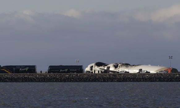 A group of people stand in front of the wreckage of Asiana Flight 214, which crashed on Saturday, July 6, 2013, as buses that were reported to be carrying passengers and family members are parked next to it on a tarmac at San Francisco International Airport .
