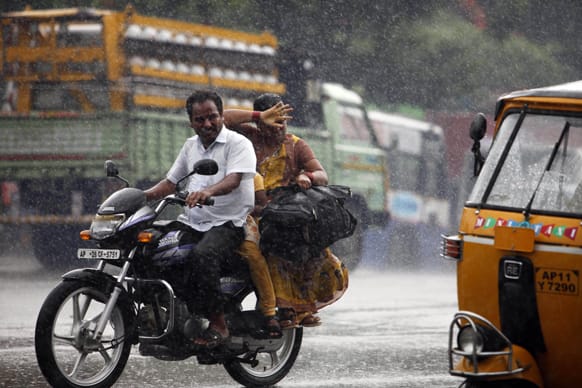 An Indian woman tries to avoid raindrops on her face as she rides behind a man on a bike in Hyderabad.