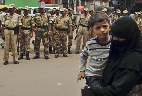 An Indian muslim woman with her child walks past paramilitary soldiers manning on a street ahead of the annual Rath Yatra or Chariot procession of Lord Jagannath in Ahmadabad.