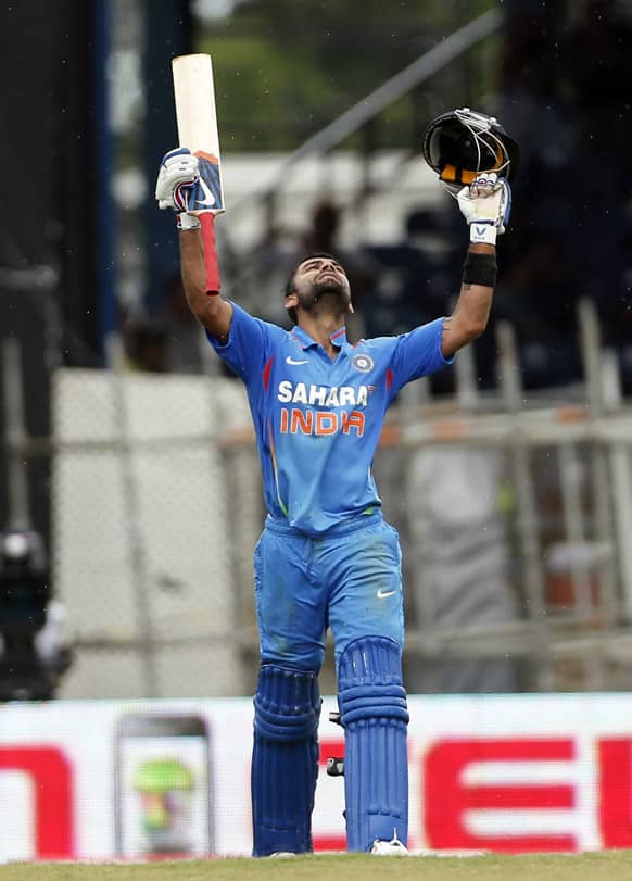 Virat Kohli raises his bat and helmet after scoring a century during the Tri-Nation Series cricket match against the West Indies in Port-of-Spain, Trinidad.