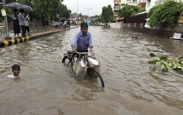 A child swims beside a man pushing his cycle past a flooded road after heavy rain lashed the city in Ahmadabad.