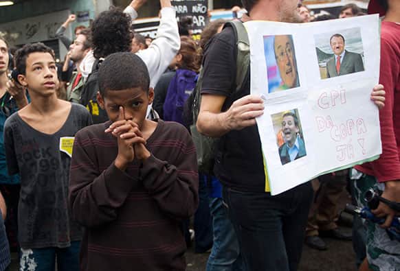 A boy gestures next to a poster with photos of FIFA President Joseph S. Blatter, left, Rio de Janeiro`s Gov. Sergio Cabral, right, and Rio`s Mayor Eduardo Paes during a protest at the Mare slum, in Rio de Janeiro, Brazil.