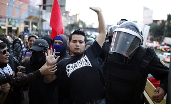 A demonstrator tries to walk on the sidewalk as police try force their way through the crowd during a march to protest against what they claim is an alleged government plan to privatize PEMEX, the state-owned oil company and also to mark the one year anniversary of the election of Mexican President.