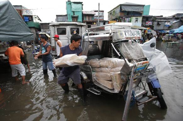 Filipino workers load goods on a tricycle along a flooded area in suburban Navotas, north of Manila.