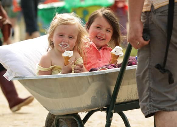 Toddlers Annabel, aged three and Olivia Green, aged five, enjoying ice-cream while being pushed along in a wheelbarrow by their father David, at the Glastonbury Festival, at Worthy Farm in Glastonbury, England.