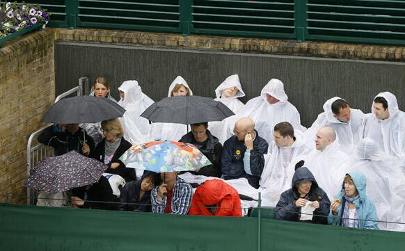 Members of the public seek shelter under umbrellas and ponchos as rain delays the start of play at the All England Lawn Tennis Championships in Wimbledon, London.