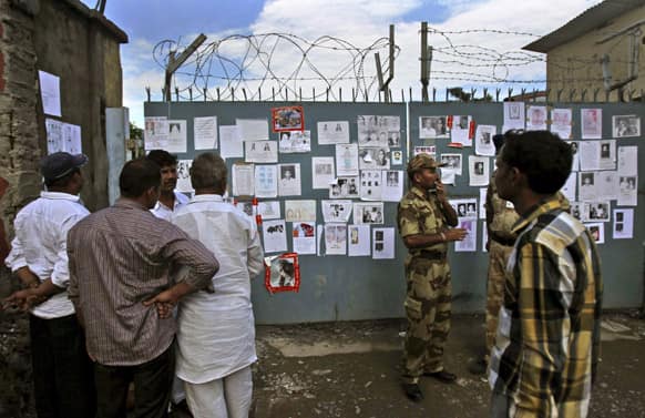 People stand near an airport gate covered with special announcements and pictures of missing people in Jollygrant, in the northern Indian state of Uttarakhand.
