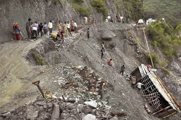 People gather near a truck carrying LPG cylinders that fell in the Bhagirathi River from a road damaged after monsoon flooding in Uttarkashi.