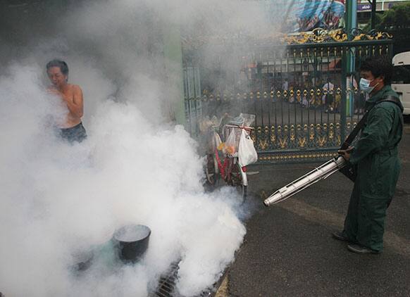 A Thai people walks away from smoke as a Bangkok Metropolitan Administration worker sprays mosquito repellent at a house in Bangkok.