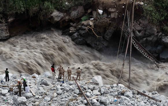 Water gushes down a river as Indian paramilitary soldiers and volunteers stand near a makeshift bridge after it was damaged hampering to evacuate the stranded pilgrims in Govindghat.