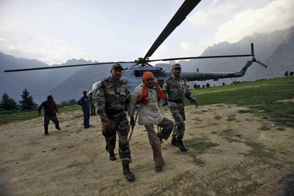 Indian army soldiers help a flood affected man after being evacuated by helicopter from the upper reaches of mountains in Joshimath.
