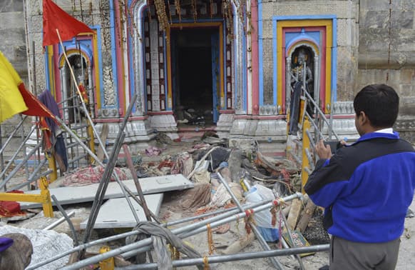 A man takes pictures as bodies of pilgrims lying in from of the Kedarnath shrine, one of the holiest of Hindu temples dedicated to Lord Shiva at Kedarnath, Uttrakhand.