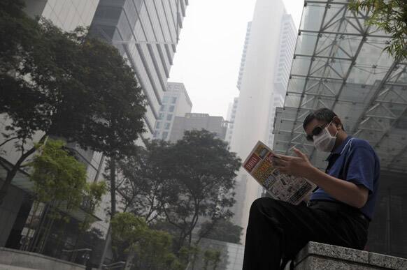 A man wears sunglasses and a mask to protect himself from a haze as he reads a newspaper in the Central Business District in Singapore.