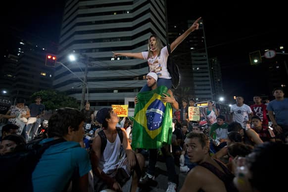 Activist Luana Carvalho, climbed on the shoulders of a demonstrator that holds a Brazilian flag, instructs a group of fellow protesters to block a street during a demonstration in Fortaleza, Brazil.