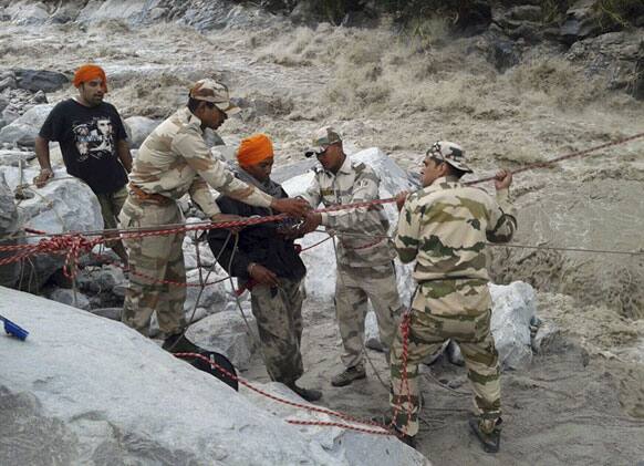 Indo-Tibetan Border Police (ITBP) use a rope to rescue stranded pilgrims, in saffron turban, cross a river swollen by flood waters at Ghangaria, in northern Indian state of Uttarakhand.