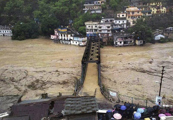People gather to watch a bridge submerged in the flooded water of the River Ganges in Rudraprayag, in northern Indian state of Uttarakhand.
