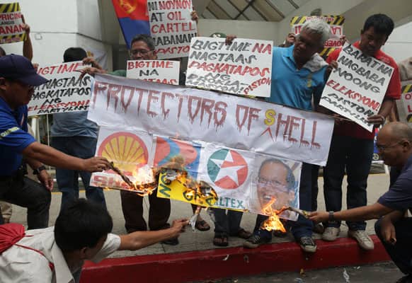 Filipino members of a drivers and operators group light a slogan bearing logos of oil companies and a picture of Philippine President Benigno Aquino III as they hold a rally outside the office of Shell at the financial district of Makati, south of Manila.