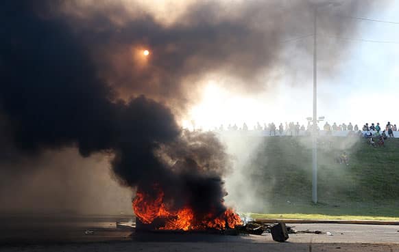 Protestors line a highway barrier in front of a burning barricade of tires near the Castelao stadium in Fortaleza, Brazil.