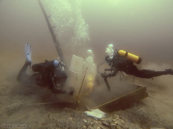 Divers inspect a hole being dug beside a wooden beam jutting from the floor of Lake Michigan that an exploration group believes may have been part of the 17th century ship the Griffin.