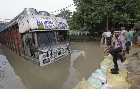 People stand near trucks partly submerged in floodwaters along the banks of the Yamuna River, in New Delhi.