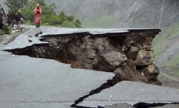 People walk on a road which was caved in after incessant rains on Rishikesh-Mana highway near Joshimath district in northern Indian state of Uttarakhand.