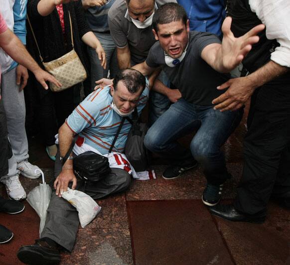 People help an injured man as Turkish riot police spray water cannon at demonstrators who remained defiant after authorities evicted activists from an Istanbul park, making clear they are taking a hardline against attempts to rekindle protests that have shaken the country, in city`s main Kizilay Square.