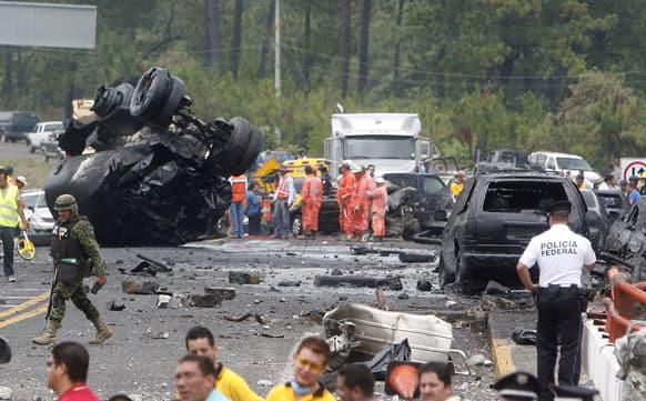 A tanker truck carrying tar sits flipped over, top left, on a highway in San Angel Zurumucapio, Mexico. Authorities say the tanker truck carrying tar slammed into a highway toll booth that had temporarily been taken over by protesting teachers.