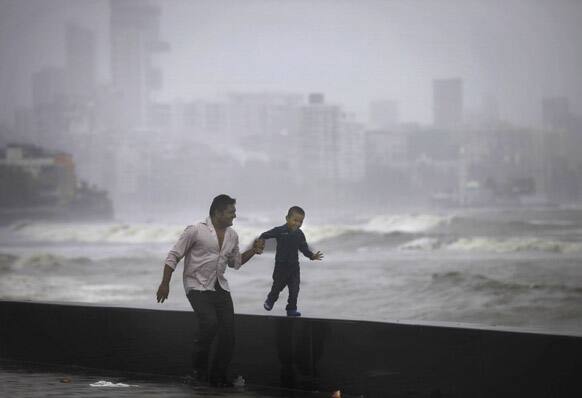 A father and son enjoy high tidal waves during monsoon rains on the Arabian Sea coast in Mumbai.