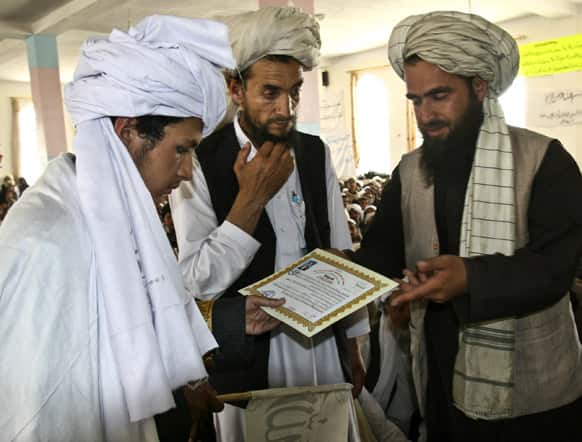 An Afghan man hands a certificate to a student as he graduates from a local Islamic school or madrassa, during a graduation ceremony at the Mazharal Olom mosque in Ghazni province west of Kabul, Afghanistan.