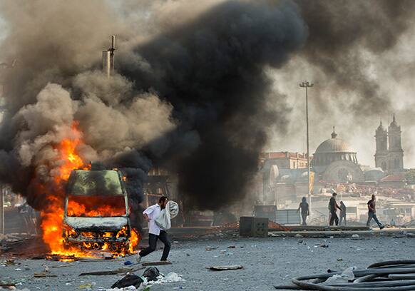 A man runs covering his face from tear gas past a burning van during clashes at the Taksim Square in Istanbul.