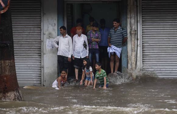 People take shelter by a wayside building as children play in water during monsoon rains in Mumbai.