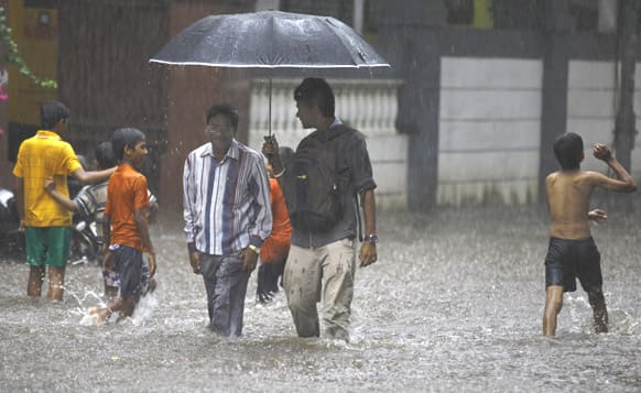 Children play as two men walk through a flooded street during monsoon rains in Mumbai. The Southwest monsoon, arrived in the city, three days ahead of schedule, according to the meteorological department.